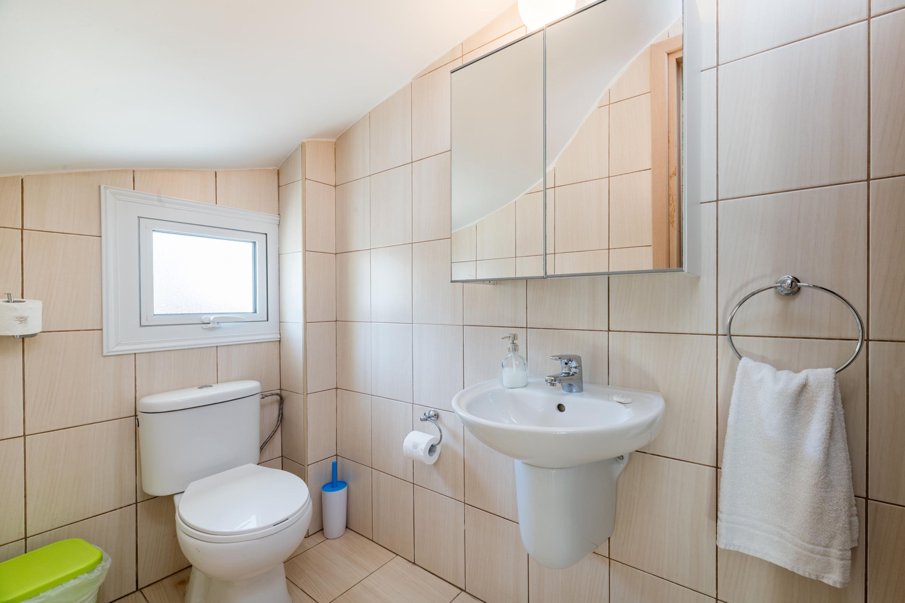 A bathroom with a toilet, sink, mirror, and towel rack.