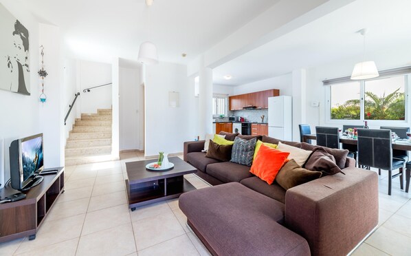 A modern living room with a sectional sofa, a flat-screen TV, and a dining area with a table and chairs. - Villa Amesta in Protaras (Paralimni)