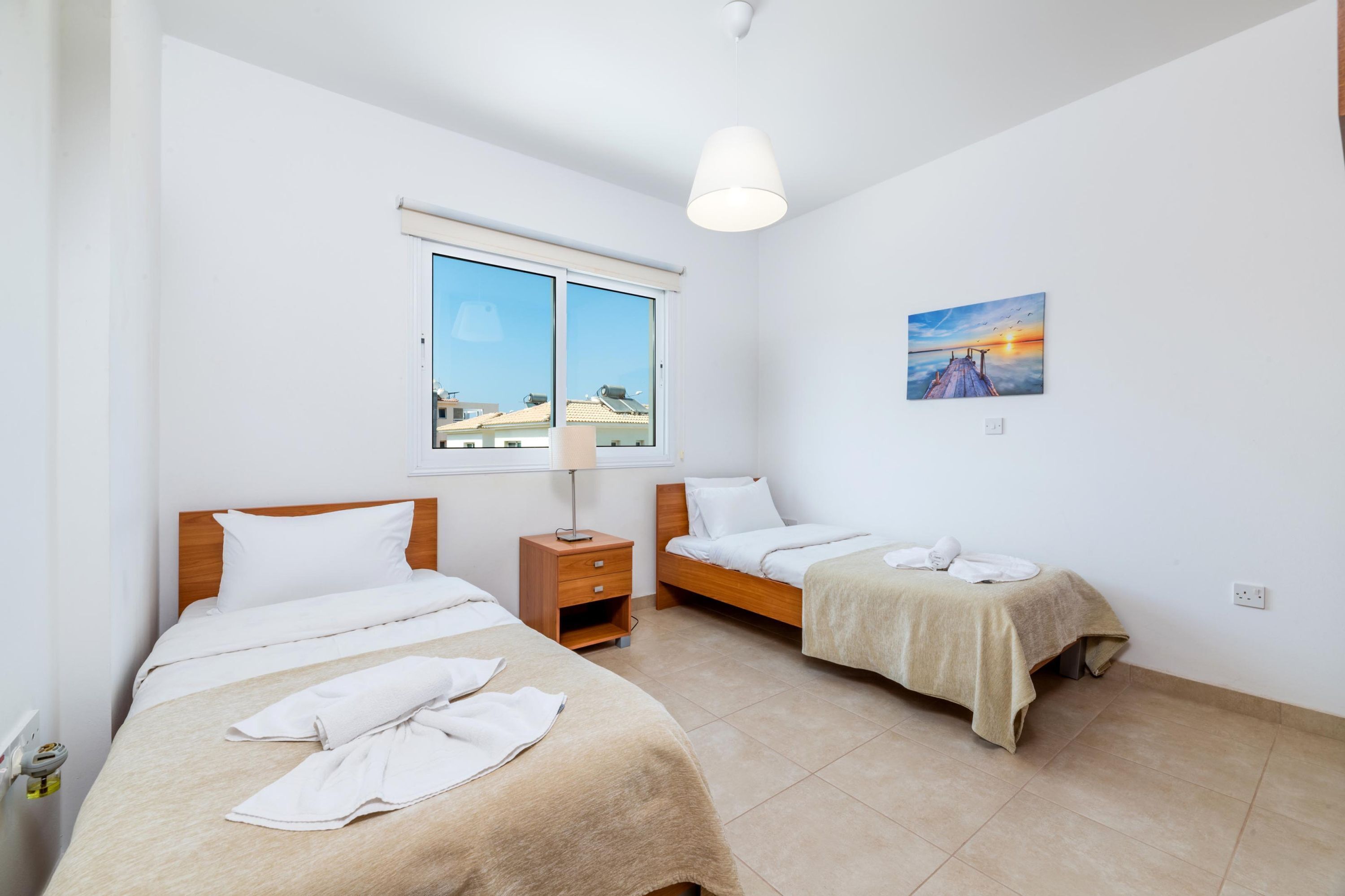 Una camera d'albergo con due letti, una finestra vista, un quadro e un comodino.