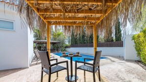 Een terras buiten met een zwembad, rieten stoelen en een tafel met eten.