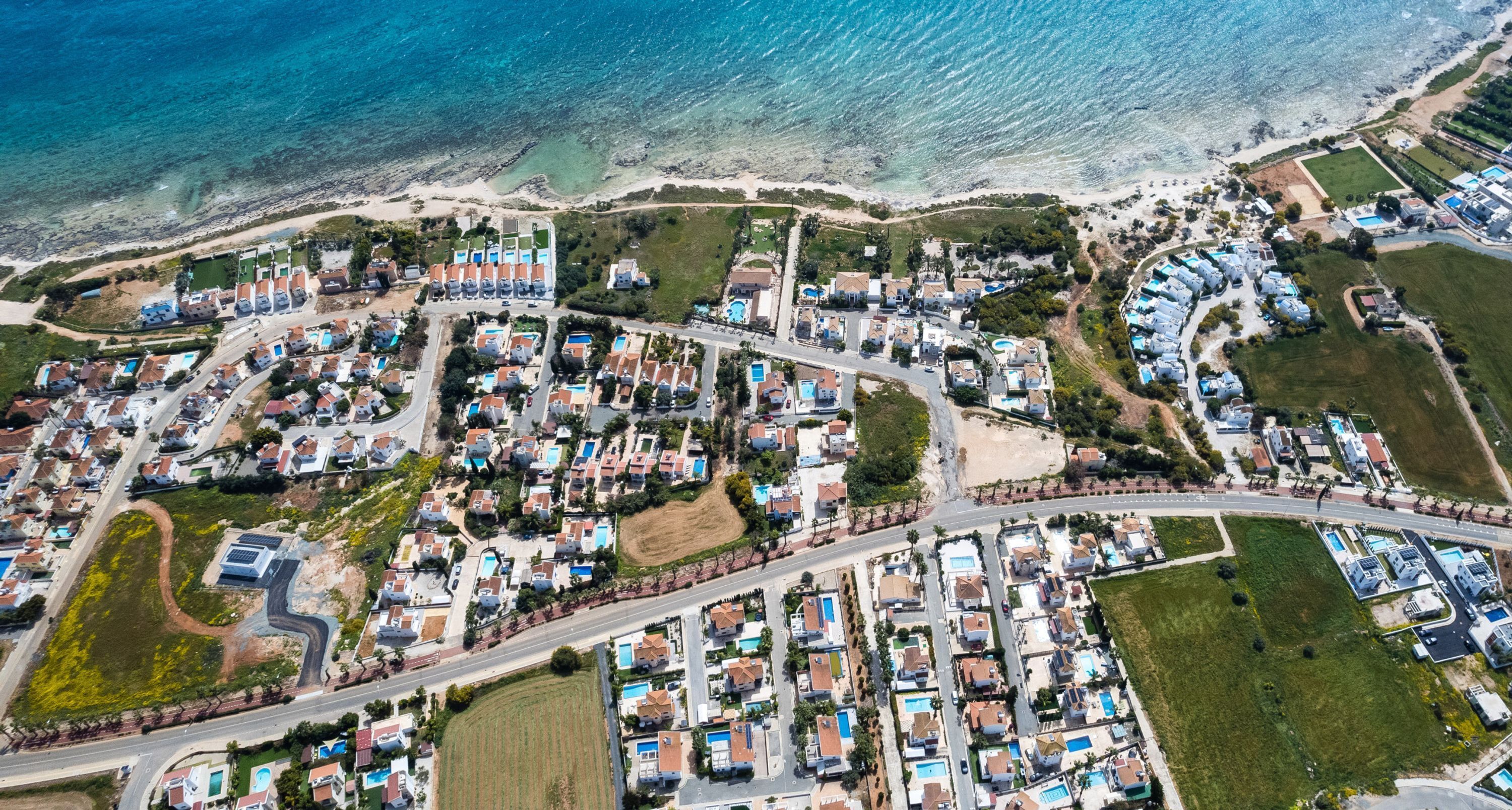 An aerial view of a coastal residential area with houses, roads, and a beach.