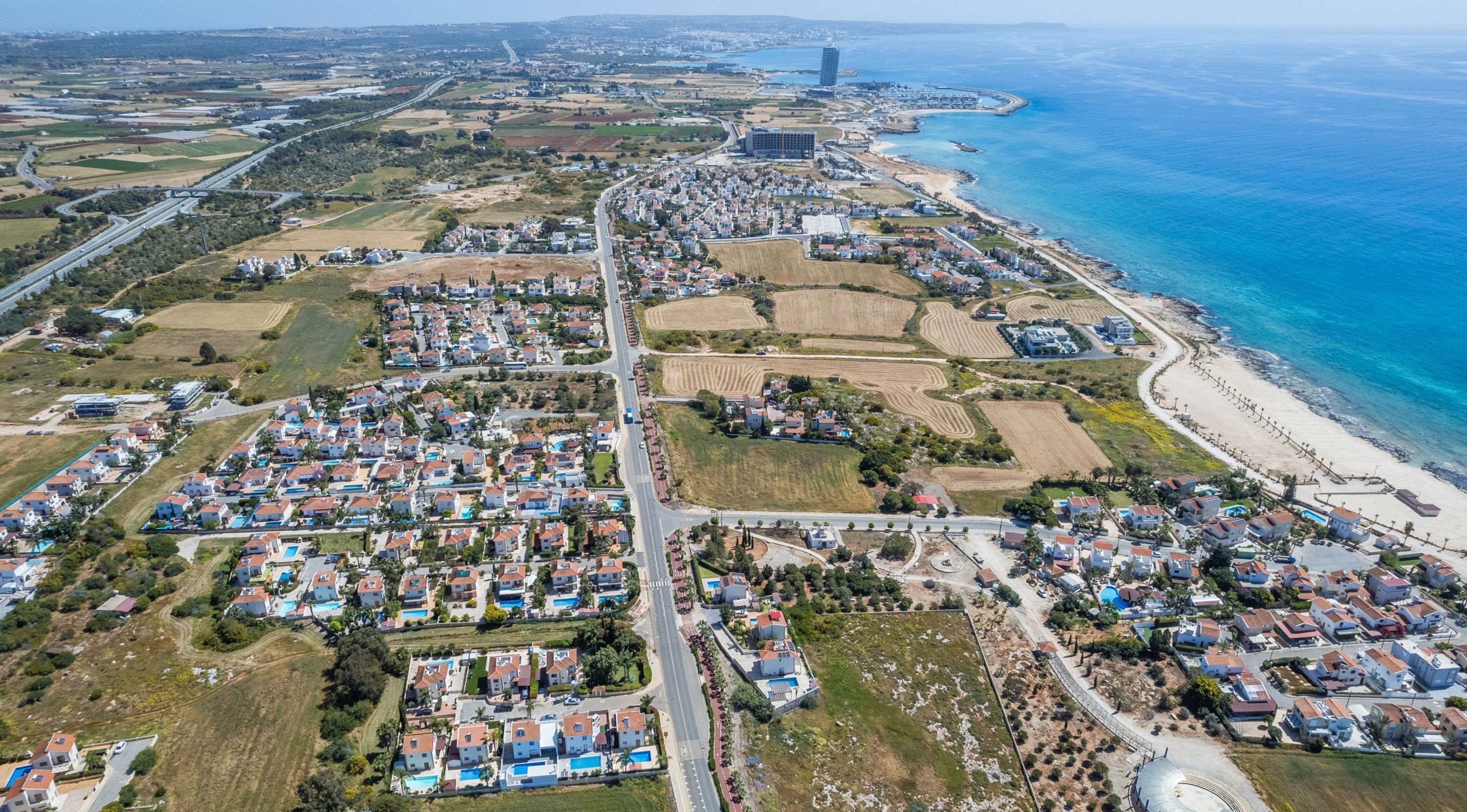 An aerial view of a coastal residential area with houses, roads, and fields.
