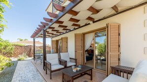An outdoor patio with wooden furniture, a stone pathway, and a covered area with wooden beams. - Elena Gardens Villa in Ayia Napa (Sotira)