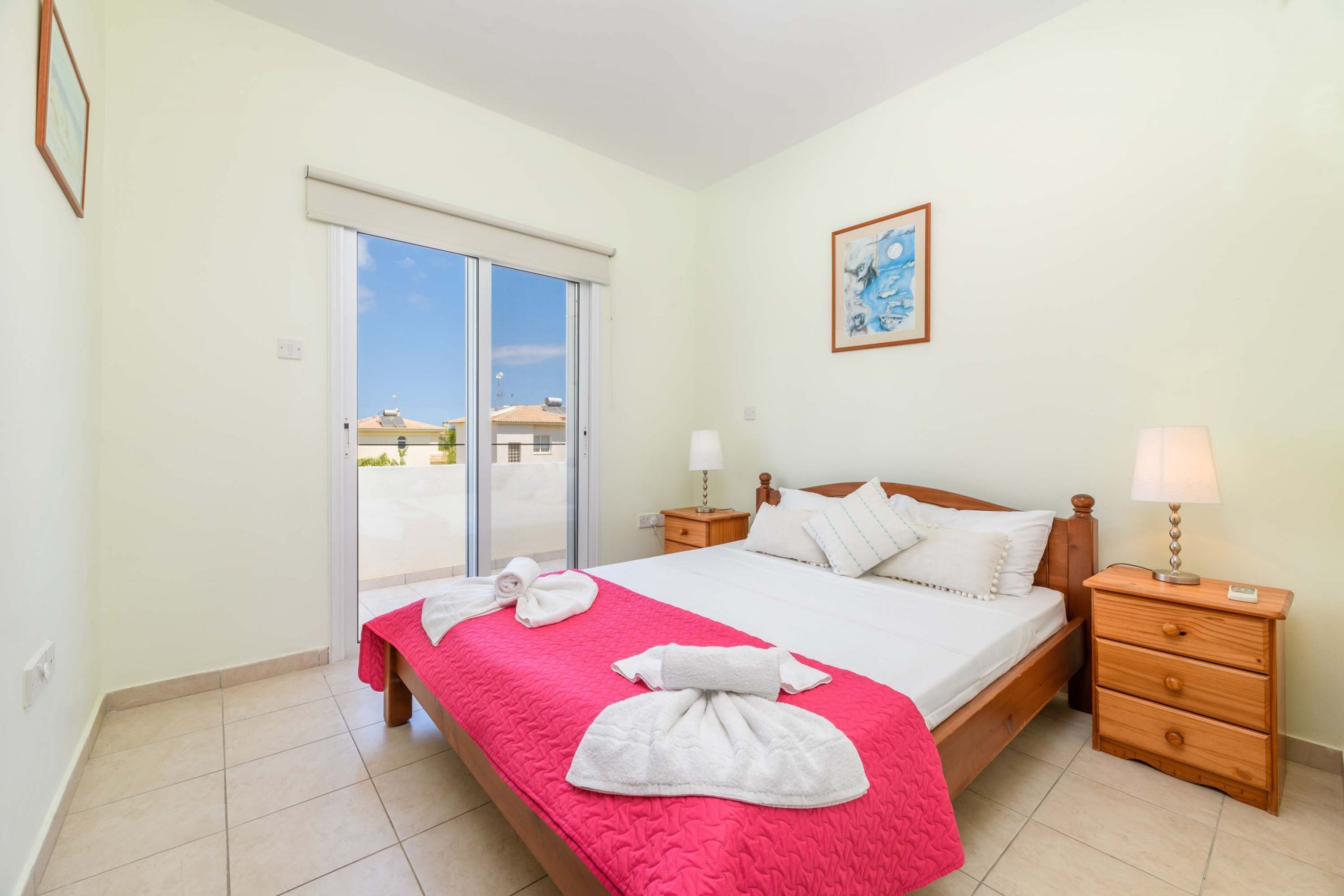 Ein Hotelzimmer mit Bett, Nachttisch, Lampe, Fenster mit Blick und einem Bild an der Wand.