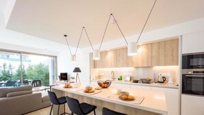 A modern kitchen with a central island, bar stools, and a dining area with a sofa. - Azure Seaview - Amber Villa (Paralimni)