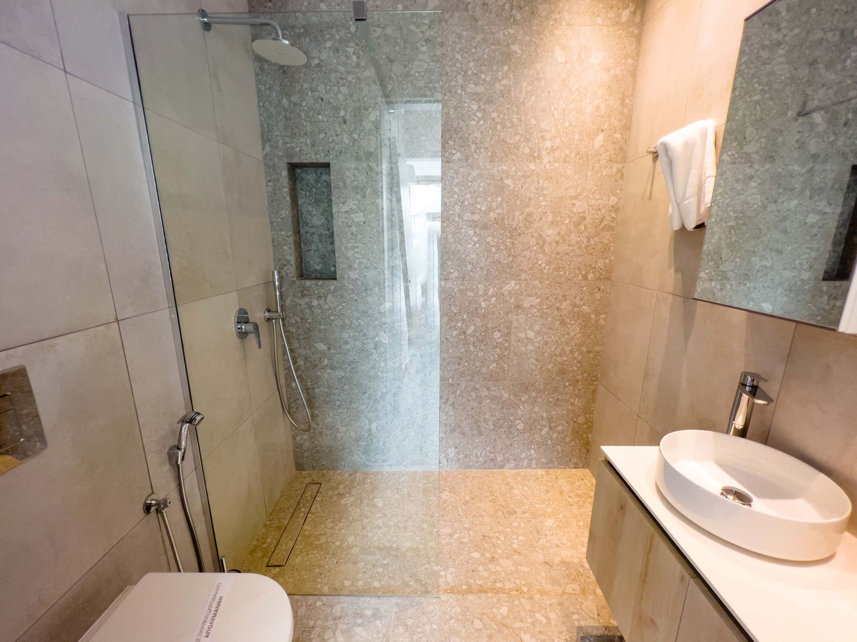 A modern bathroom with a glass-enclosed shower, a white sink, and a large mirror.