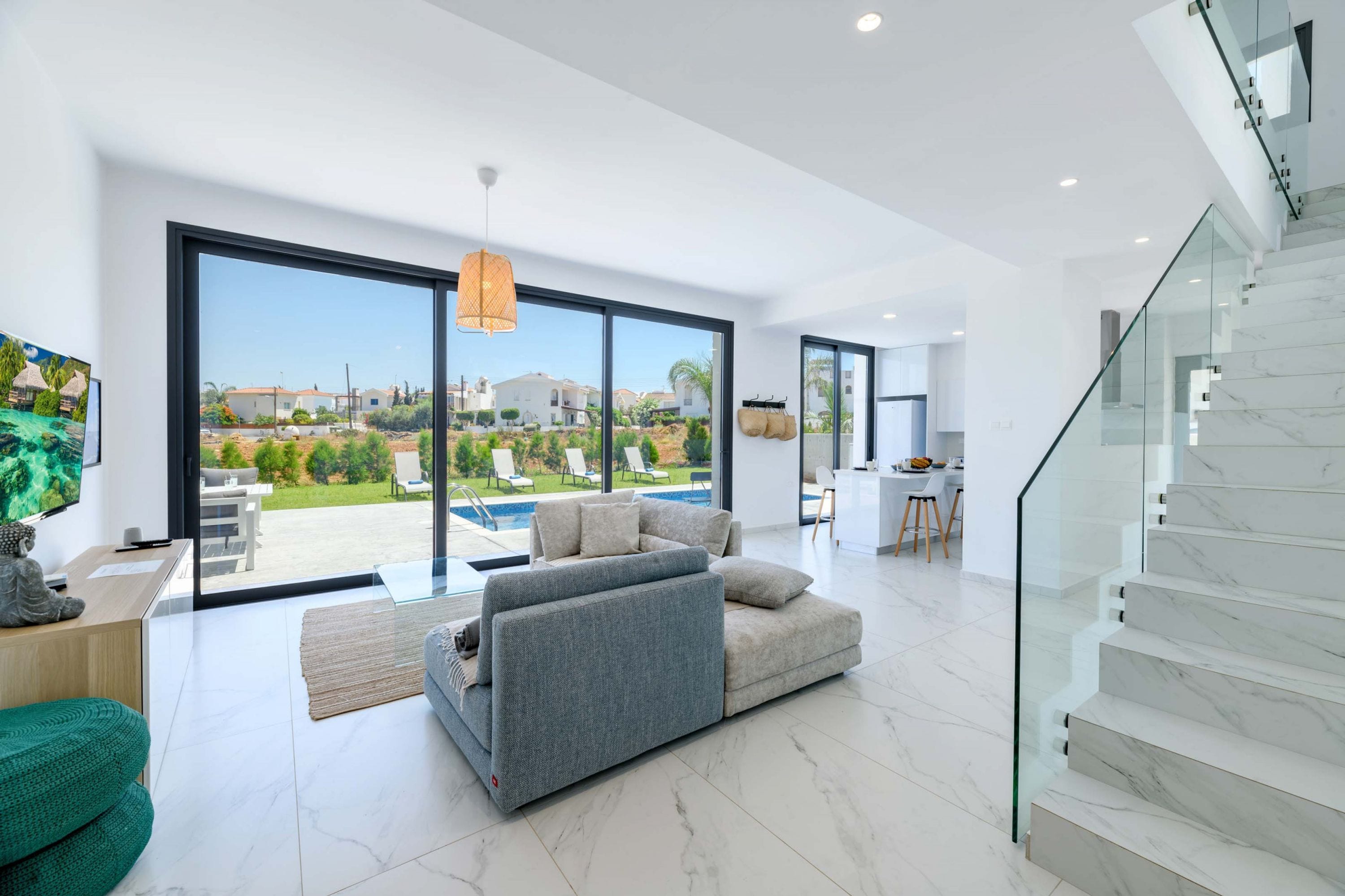 A modern living room with a large sliding glass door leading to a pool area, a grey sectional sofa, and a staircase with marble steps.
