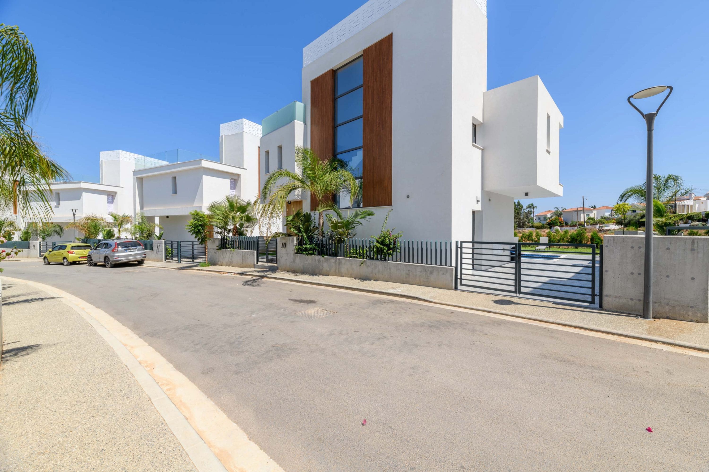 Una zona residencial moderna con edificios blancos, una entrada con reja y automóviles estacionados.
