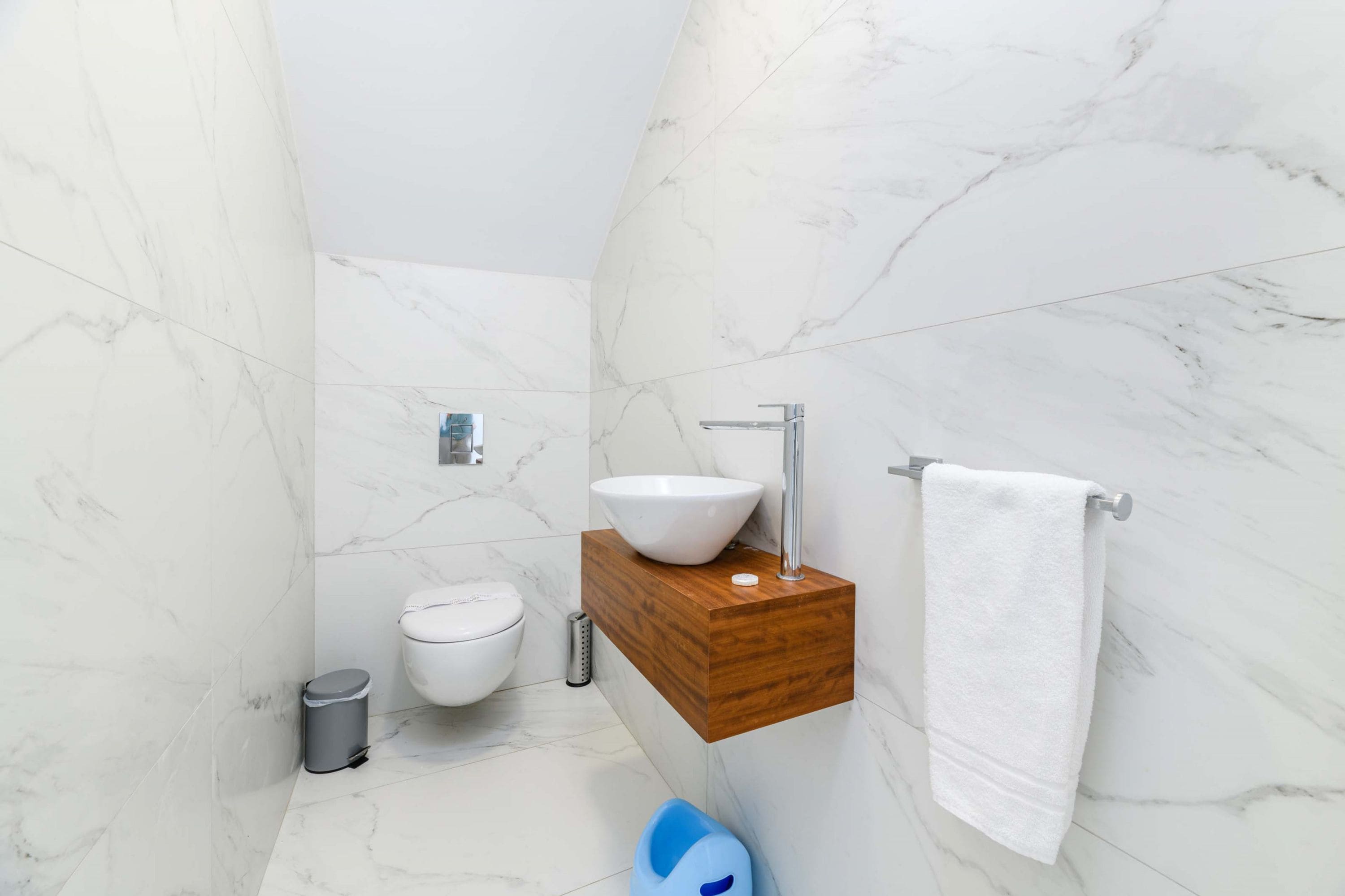 A bathroom with a marble floor, a wooden vanity with a white sink, a toilet, and a trash can.