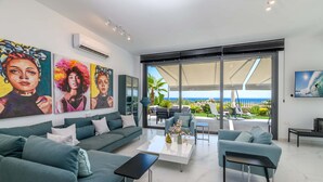 A modern living room with teal sofas, a coffee table, and artwork on the walls. - By The Beach - Emerald Seaview Villa (Paralimni)