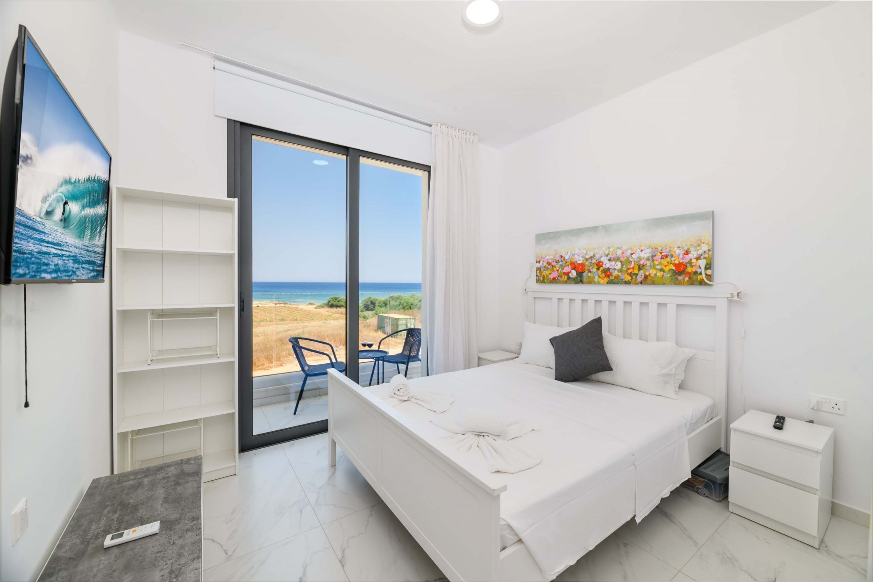 Een slaapkamer met een bed, een schilderij, een televisie en uitzicht op het strand.