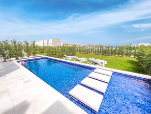 A swimming pool with clear blue water, surrounded by white lounge chairs and a grassy area. - Azure Seaview - Jade Villa (Paralimni)