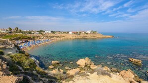 A coastal beach with clear waters, rocky shore, and beach umbrellas. - Azure Seaview - Jade Villa (Paralimni)