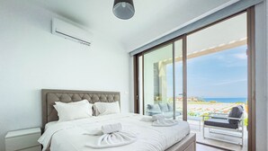 A modern hotel room with a large bed, a glass door leading to a balcony with a beach view. - Azure Seaview - Jade Villa (Paralimni)