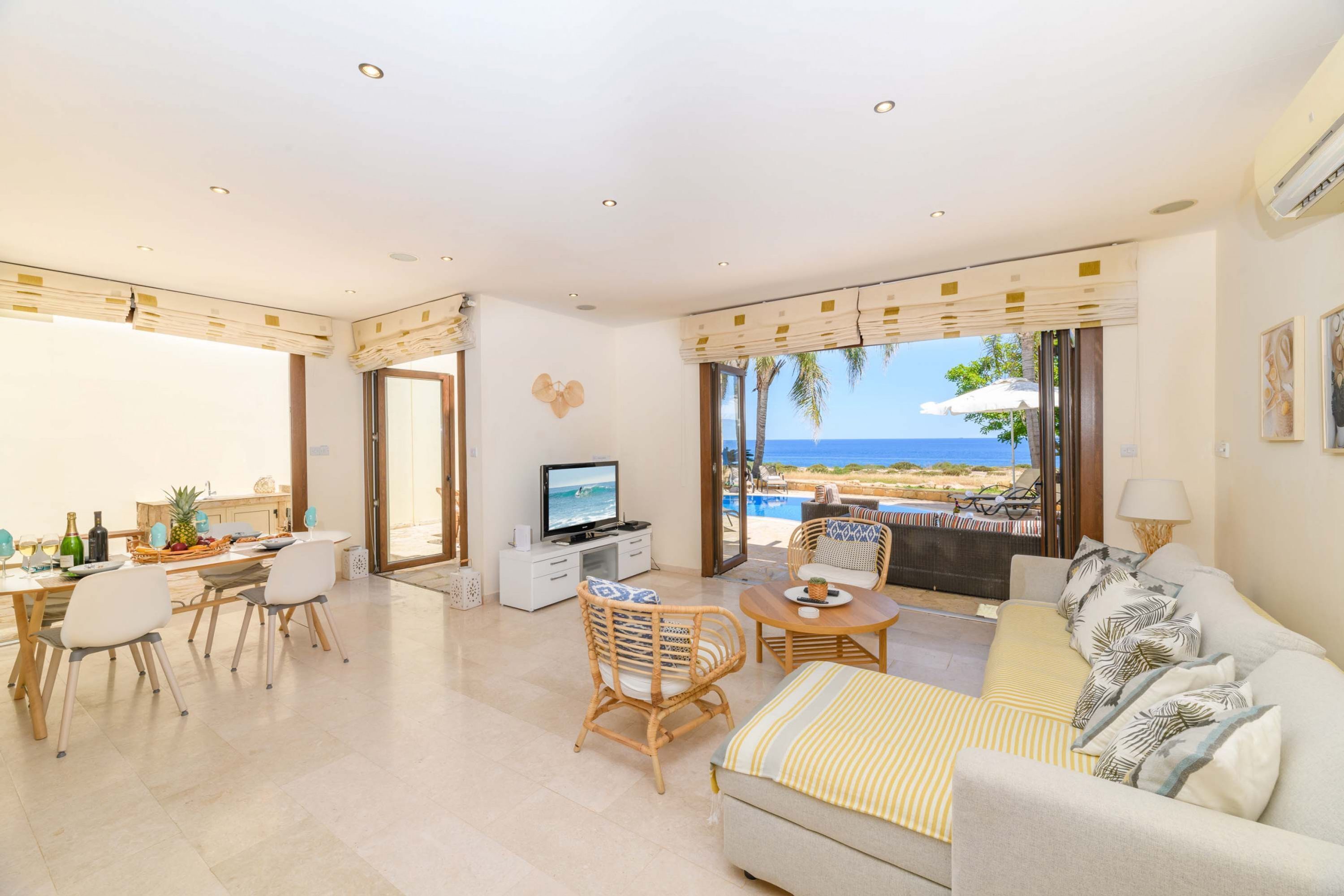 A spacious living area with a television, dining table, and seating. A large window offers a view of the ocean.