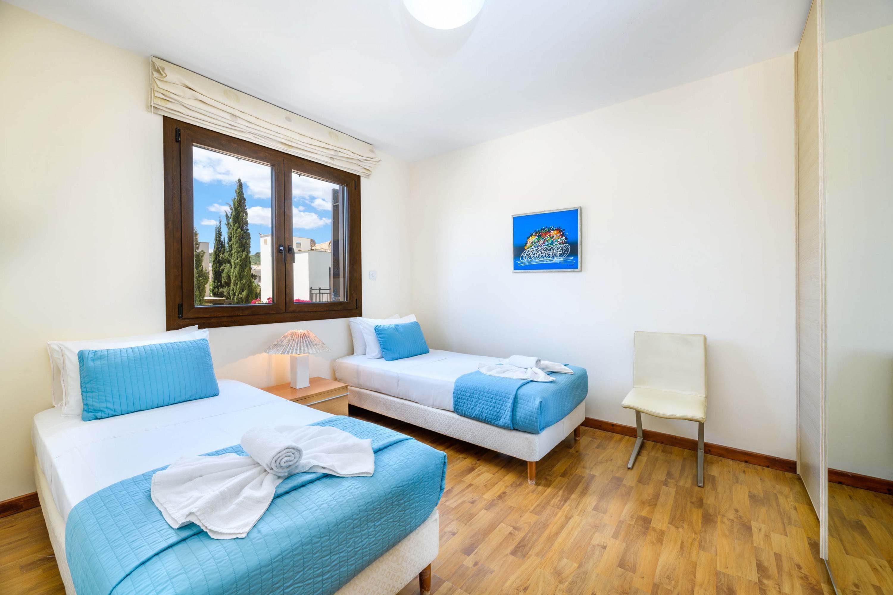 Ein Schlafzimmer mit zwei Betten, einem Sessel, einem Fenster mit Blick auf Bäume und einem Bild an der Wand.