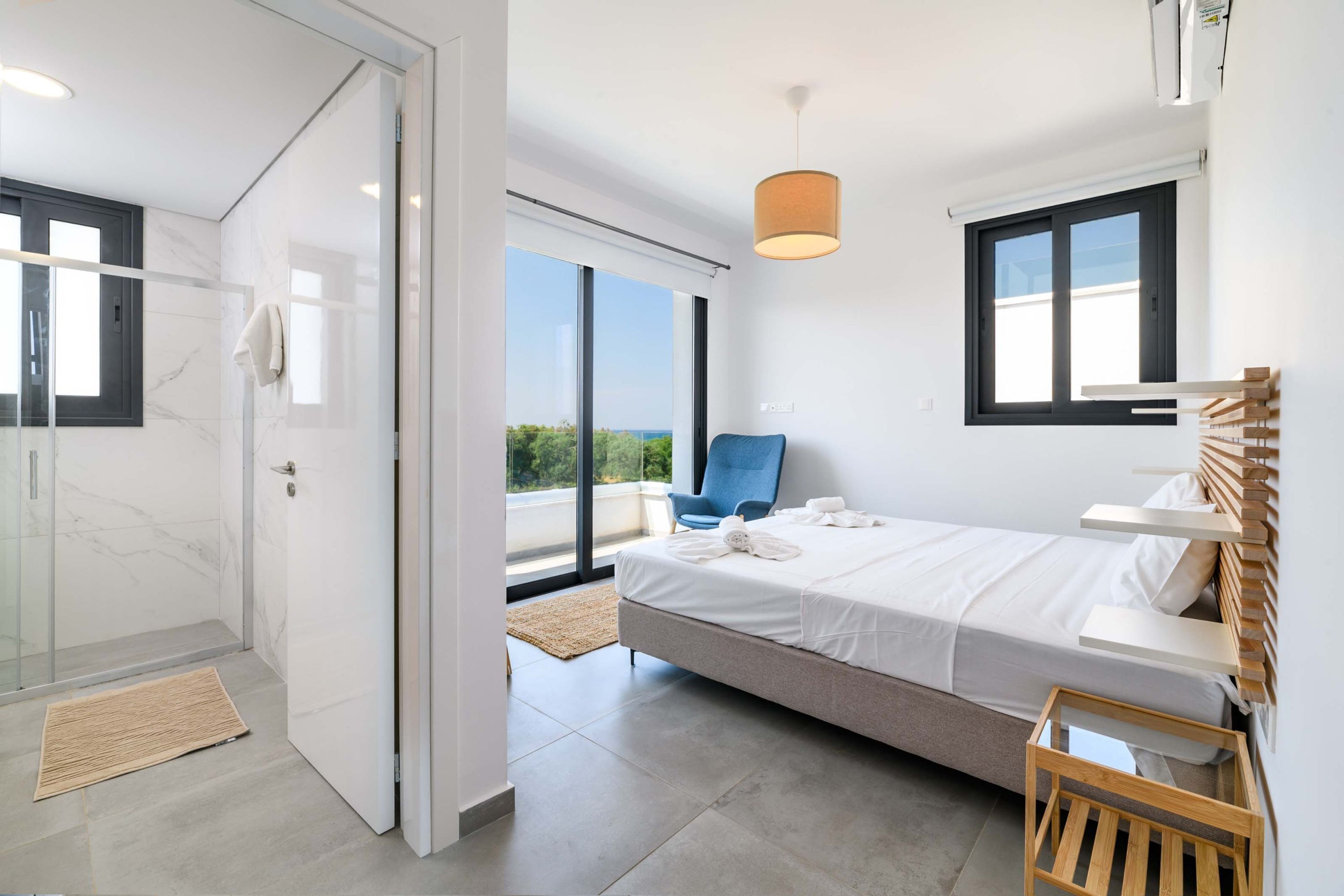 Ein modernes Schlafzimmer mit Bett, Stuhl, Nachttisch und Blick ins Freie.