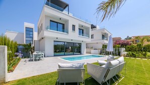 Una casa moderna de dos pisos con piscina, mobiliario exterior y un jardín bien cuidado.