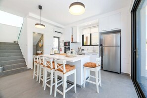 A modern kitchen with a central island, white cabinetry, stainless steel appliances, and a glass door leading to a balcony. - By The Beach - Sea Pearl Villa (Paralimni)