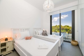 Een moderne slaapkamer met twee bedden, een nachtkastje, een kroonluchter en een balkon met uitzicht op groen.