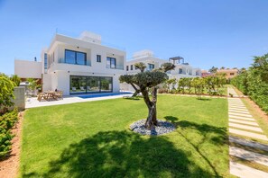 A modern two-story house with a large glass front, a swimming pool, and a well-maintained lawn. - By The Beach - Sea Pearl Villa (Paralimni)
