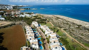 An aerial view of a coastal resort with multiple villas, a sandy beach, and a clear blue sea. - Villa Greco Mare 20 (Paralimni)