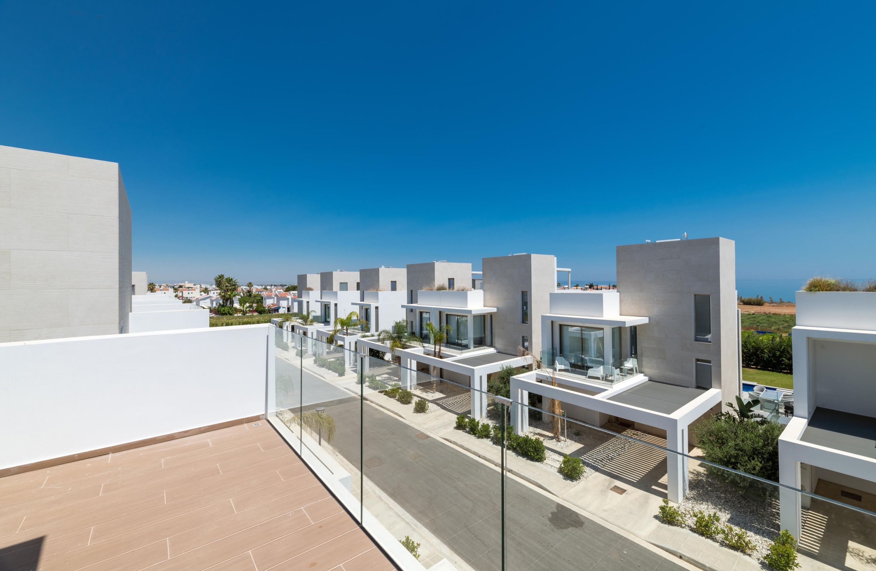 A modern residential complex with multiple white buildings, a clear blue sky, and a view of the sea.