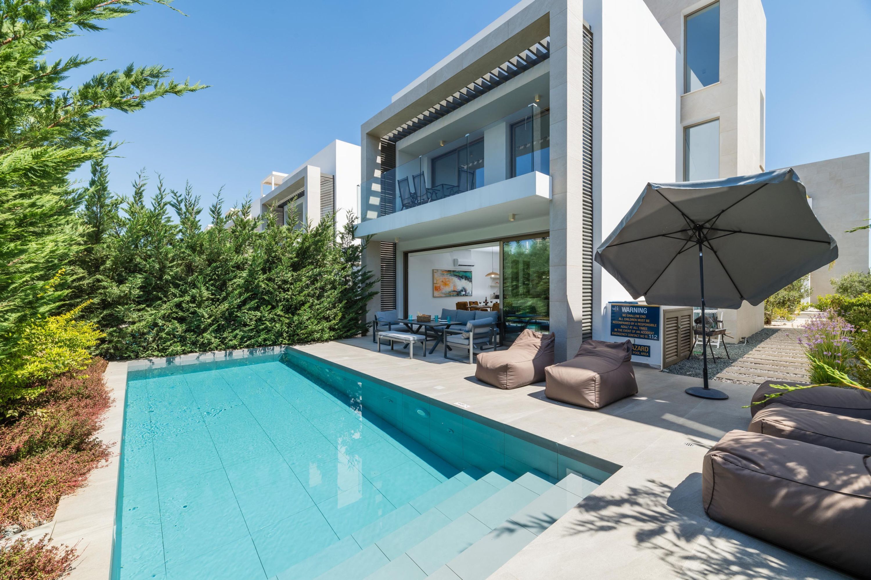 Une maison moderne à deux étages dotée d’une piscine, d’un espace salon extérieur et d’un grand parasol.