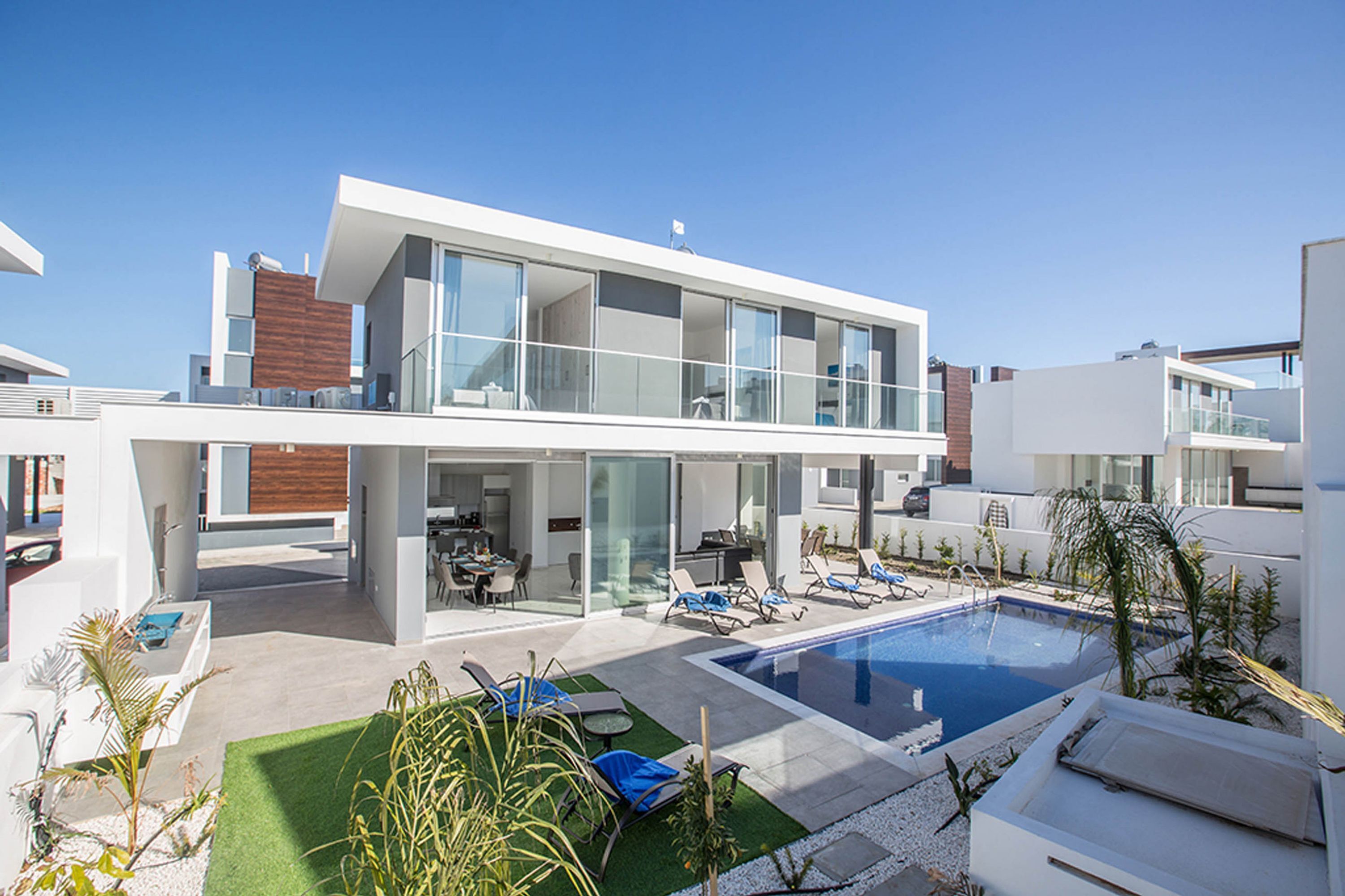 Una casa moderna de dos pisos con piscina, mobiliario exterior y zona de patio.
