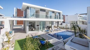 Una casa moderna de dos pisos con piscina, mobiliario exterior y zona de patio.
