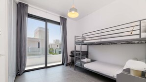 Une chambre d’hôtel moderne équipée d’un lit superposé, d’un bureau, d’une chaise et d’une grande fenêtre avec des rideaux.