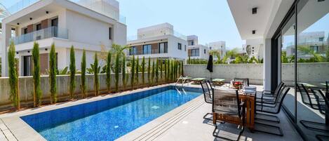 A modern outdoor swimming pool area with a dining setup.