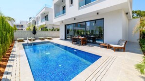 Un espace piscine moderne comprenant une piscine rectangulaire, des chaises longues et une table à manger.