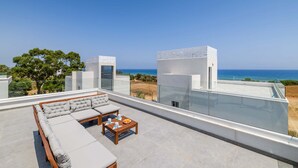 Une terrasse sur le toit, aménagée avec un canapé, une table et des chaises, d’où l’on a une vue sur une plage et l’océan.