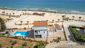 En ejendom ved stranden med pool, overdækket terrasse og havudsigt.