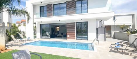 Uma casa moderna de dois andares com piscina, área de estar externa e um gramado bem cuidado.