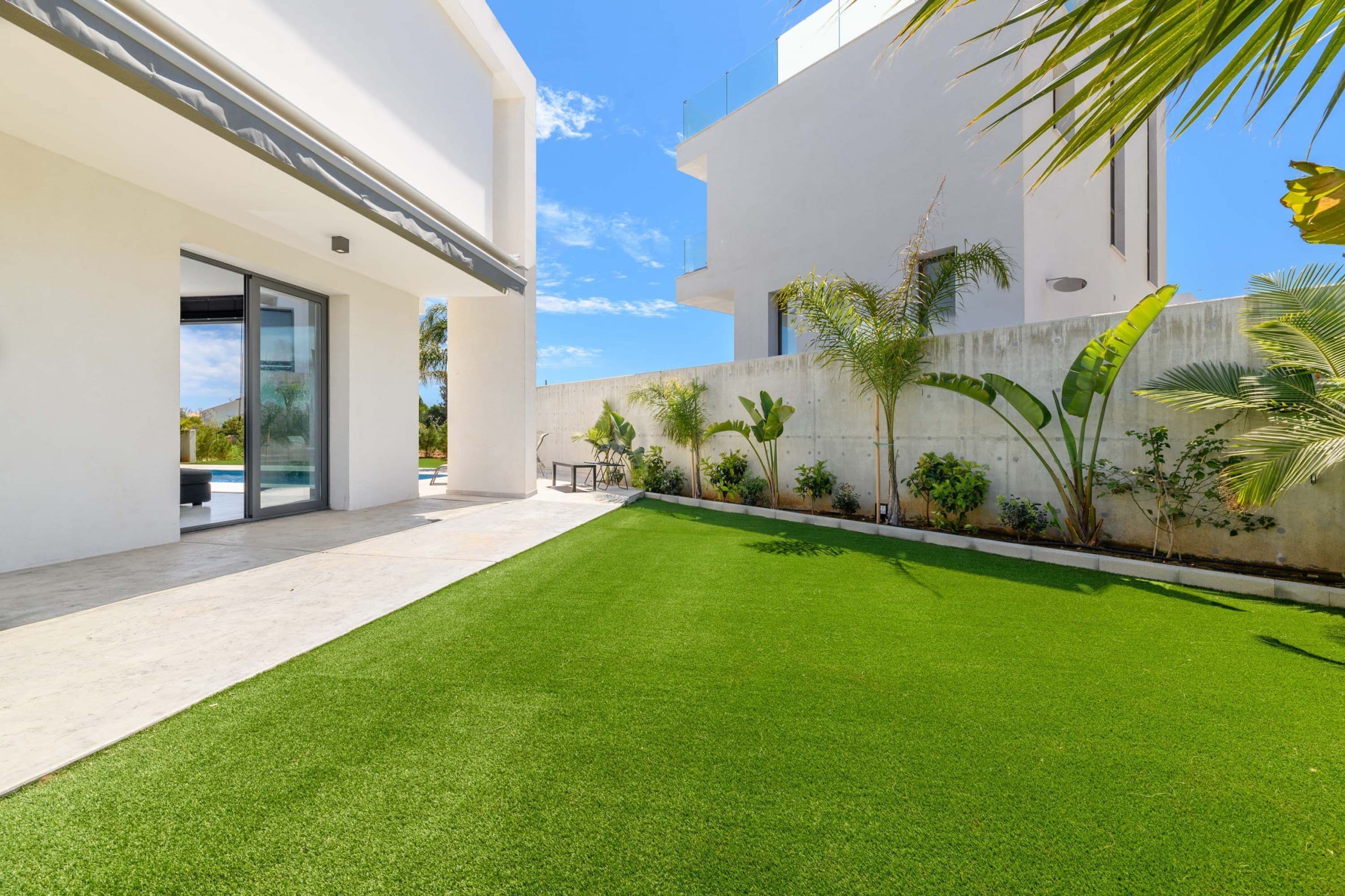 A modern building with a flat roof, a flat facade, and a small courtyard with artificial grass and potted plants.