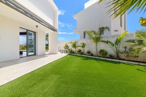 Un edificio moderno con techo plano, fachada plana y un pequeño patio con césped artificial y plantas en macetas.