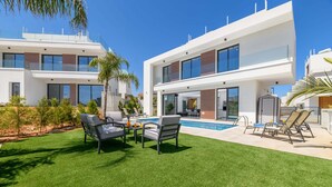Una casa moderna de dos pisos con piscina, mobiliario exterior y un césped bien cuidado.