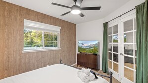 Un dormitorio con cama, ventilador de techo, televisor, ventana y puerta corrediza.