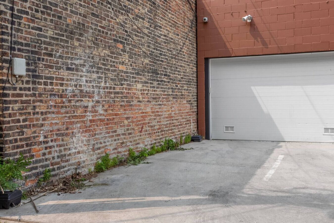 A brick building with a garage door, a concrete driveway, and a utility box on the wall.