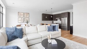 Una sala de estar moderna con un sofá blanco, una mesa de centro negra y una cocina al fondo.