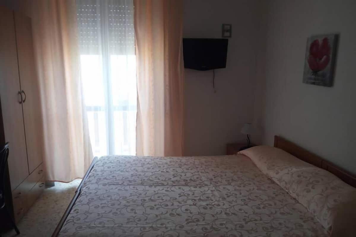 Un dormitorio con cama, televisión en la pared y ventana con cortinas.