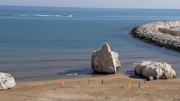 Uma praia com águas azul-claras, rochas grandes e uma faixa de areia.