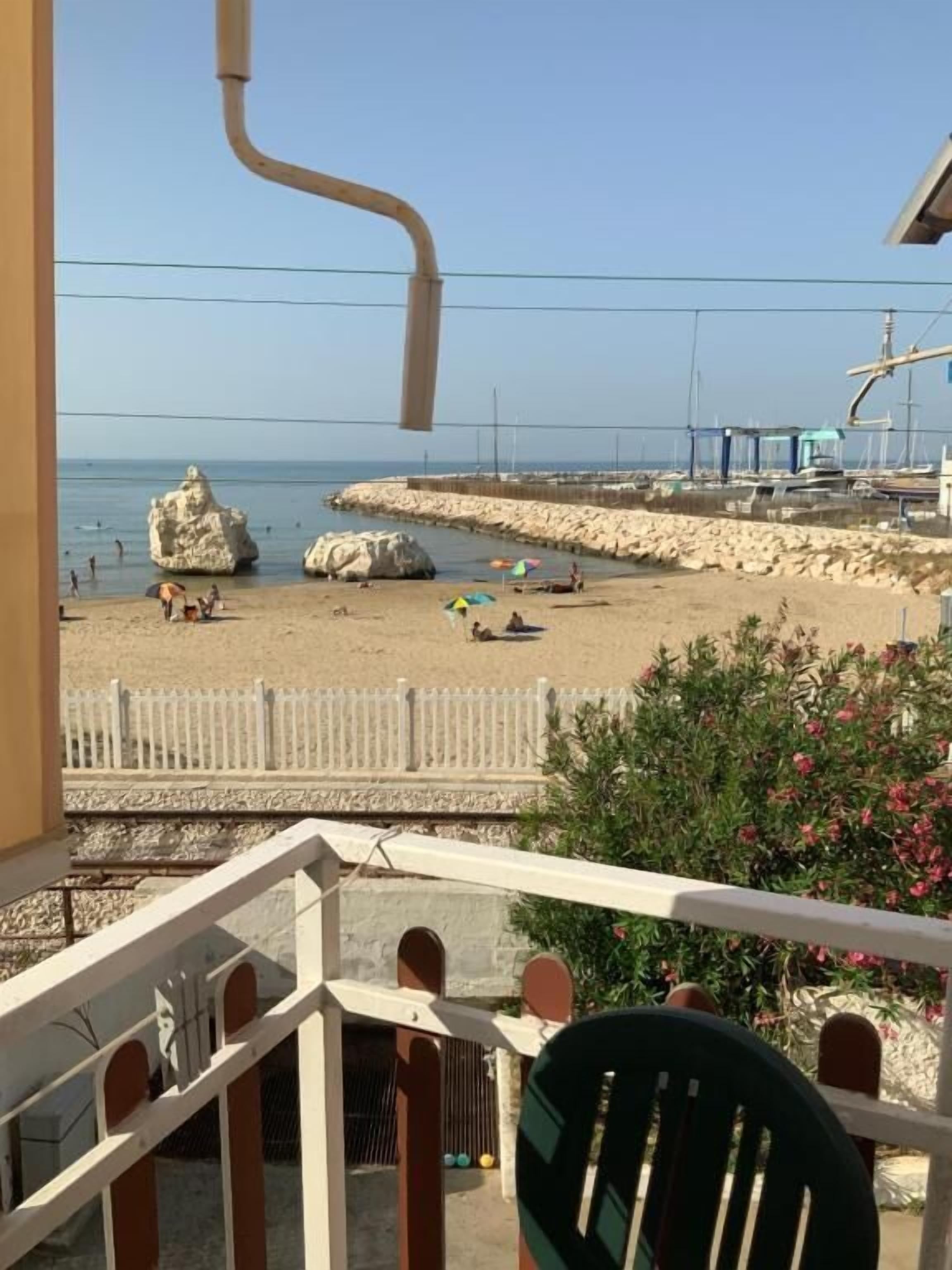 A balcony with a view of a beach, a white fence, and a rock formation.