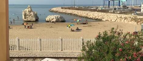 A balcony with a view of a beach, a white fence, and a rock formation.