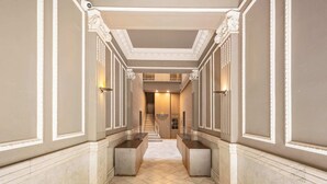 Un corridoio con pavimento in marmo, rivestimenti bianchi in legno e una scalinata centrale che conduce a un piano superiore.
