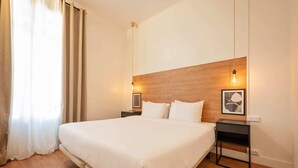 Camera d'albergo con un letto grande, una testiera in legno, comodini e opere d'arte.