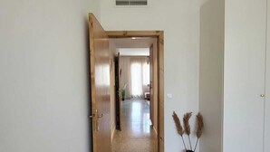 Un couloir avec une porte en bois, une armoire blanche et un vase contenant des plantes séchées.