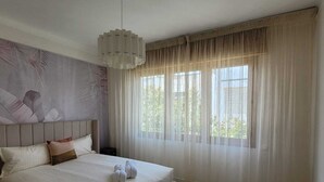 Une chambre à coucher avec un lit, une tête de lit, un luminaire suspendu et des rideaux légers.
